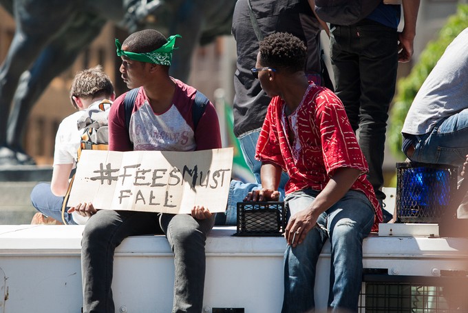 Photo of two people, one with a placard saying fees must fall