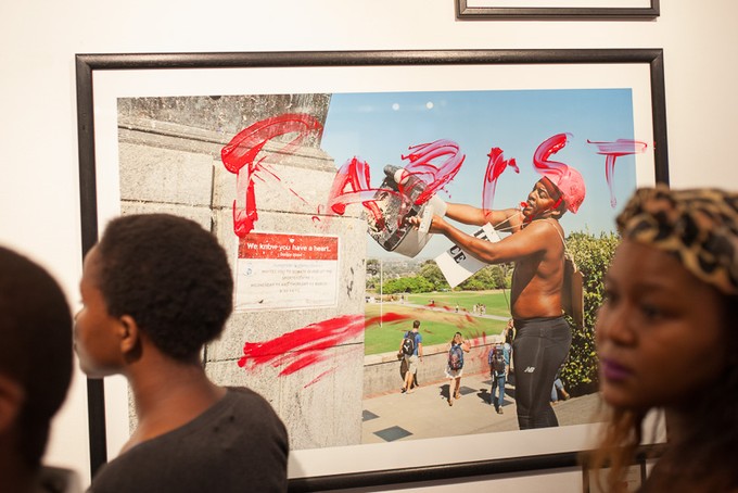 People look at photos in the exhibition, one of which is of Chumani Maxwele