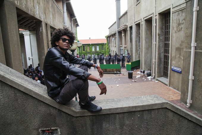 Photo of a young man sitting with security men with shields in the background