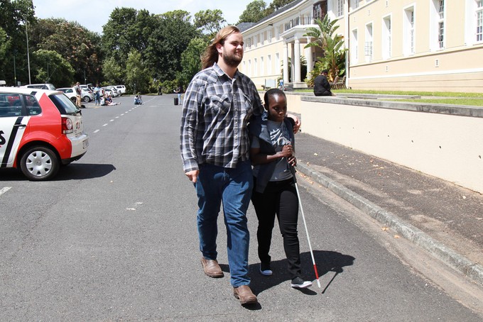 Photo ofJoan Byamugisha being led by her friend James Harvey. 