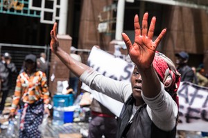 A women lifts her hands that was dippid in red coloured water which is used by the police water canon. She said that it resembles “blood”.