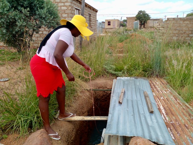 Photo of a woman drawing water from a hole in the ground