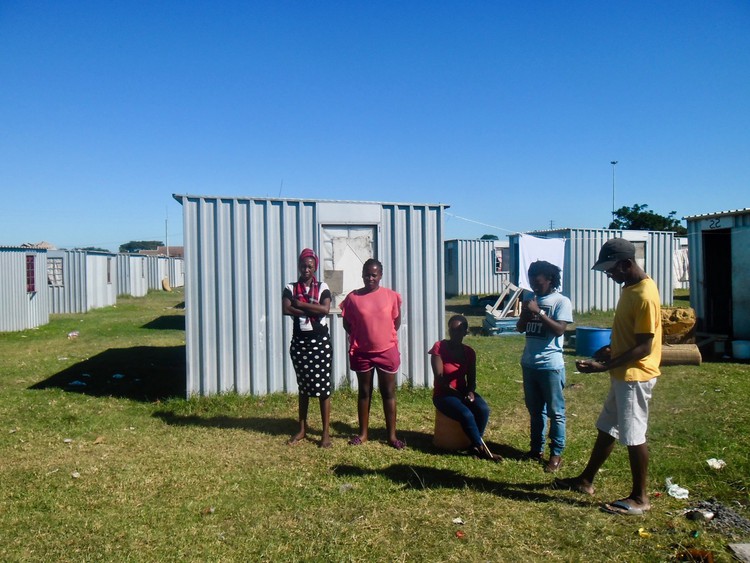 Photo of a group of people in front of tin shacks