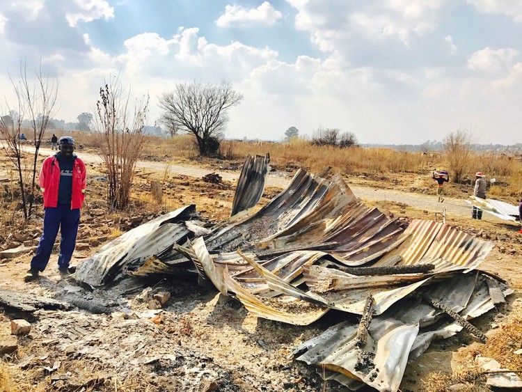 Photo of man standing next to burnt shack