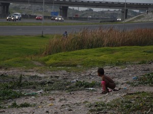 Photo of boy quite far from camera defecating with cars driving by on the N2