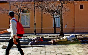 Photo of two men sleeping on a pavement and a passerby