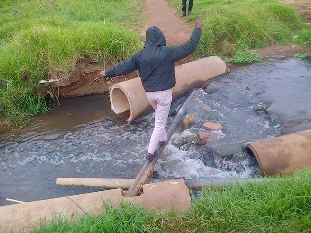 Photo of a man walking on. a pole across a stream