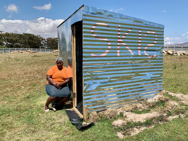 Photo of a woman sitting next to a shack