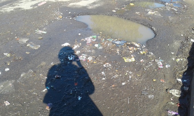 Photo of shadow over flooded, potholed road.