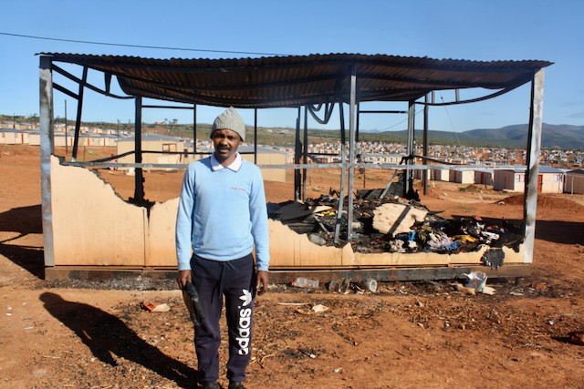 A man in front of a burnt out house