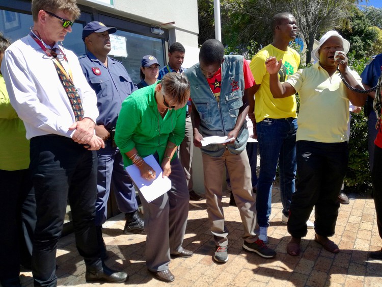 Photo of a person signing a document in front of protesters