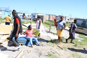 Photo of woman sitting on mattress in ruins of shack