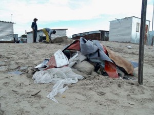 Photo of an empty plot with shacks behind